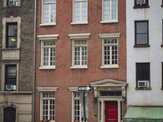 Historic brick townhouses in Greenwich Village, New York City, with white-trimmed windows and a red front door on a quiet tree-lined street
