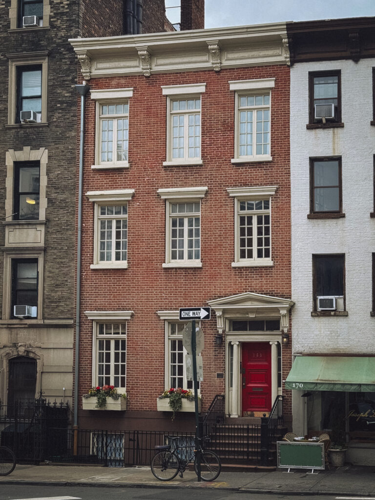 Historic brick townhouses in Greenwich Village, New York City, with white-trimmed windows and a red front door on a quiet tree-lined street